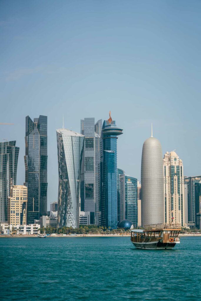 Panoramic view of Doha West Bay skyline with modern skyscrapers and a traditional dhow boat in the foreground.
